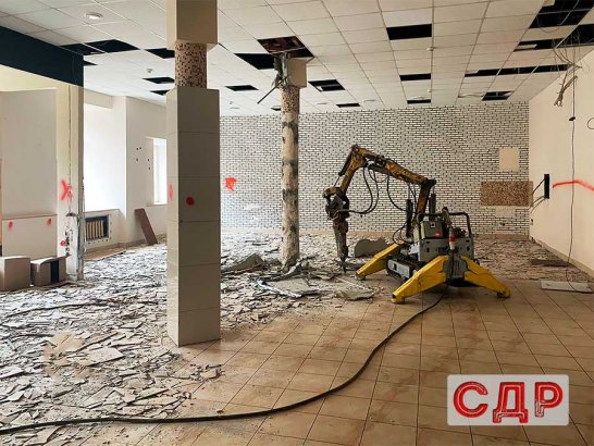 Демонтажный робот разбивает плиточный пол и бетонную стяжку.